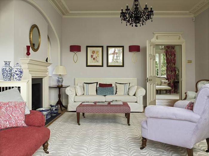 a formal, elegant drawing room with limestone chimneypiece,  silk rug, an eclectic mix of antique pieces & two large black glass chandeliers