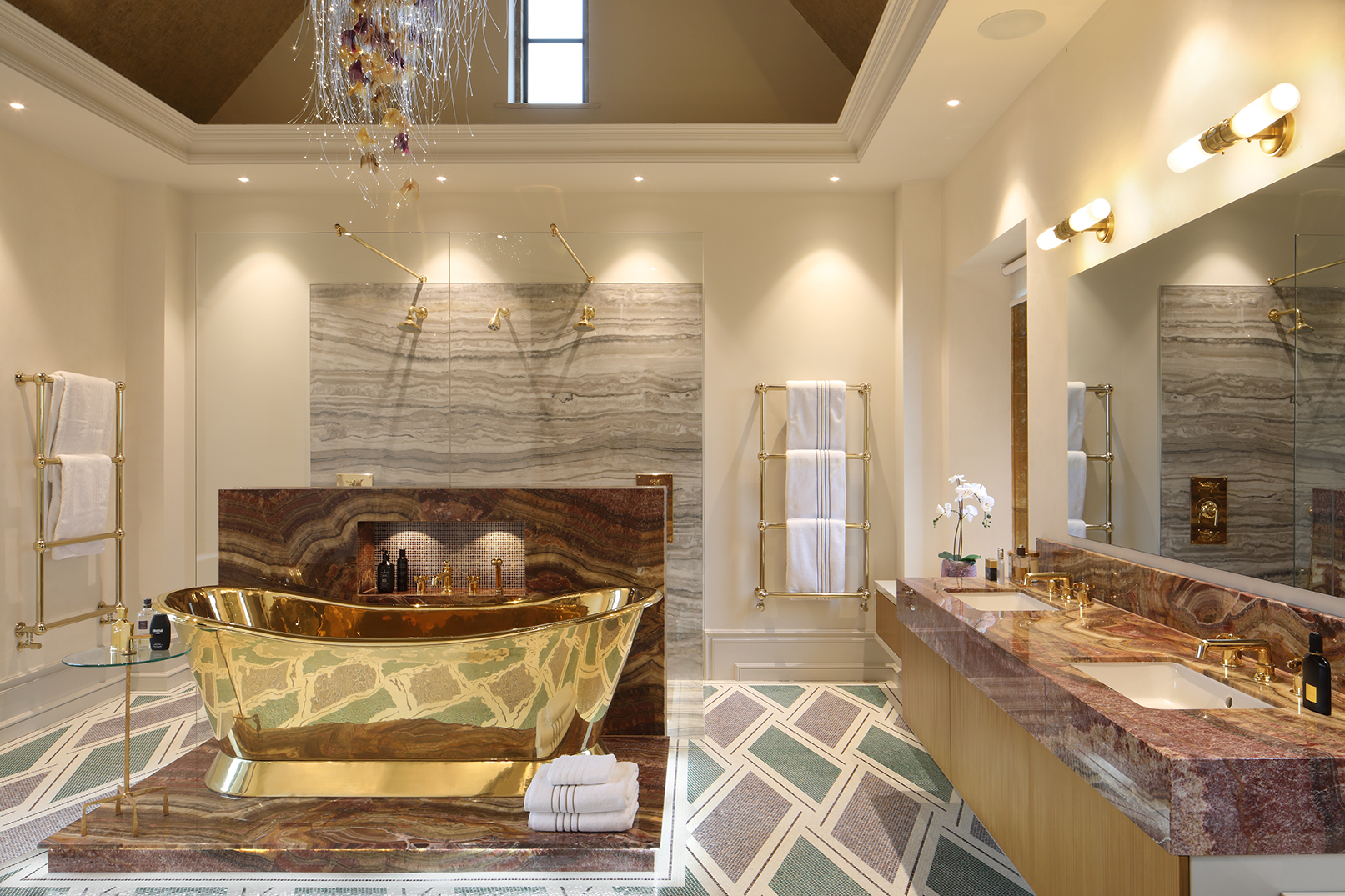 A gold bath on a marble podium is the focal point of the mosaic floored ensuite bathroom, which also includes twin basins in a marble vanity unit and a shower cubicle with three shower heads.