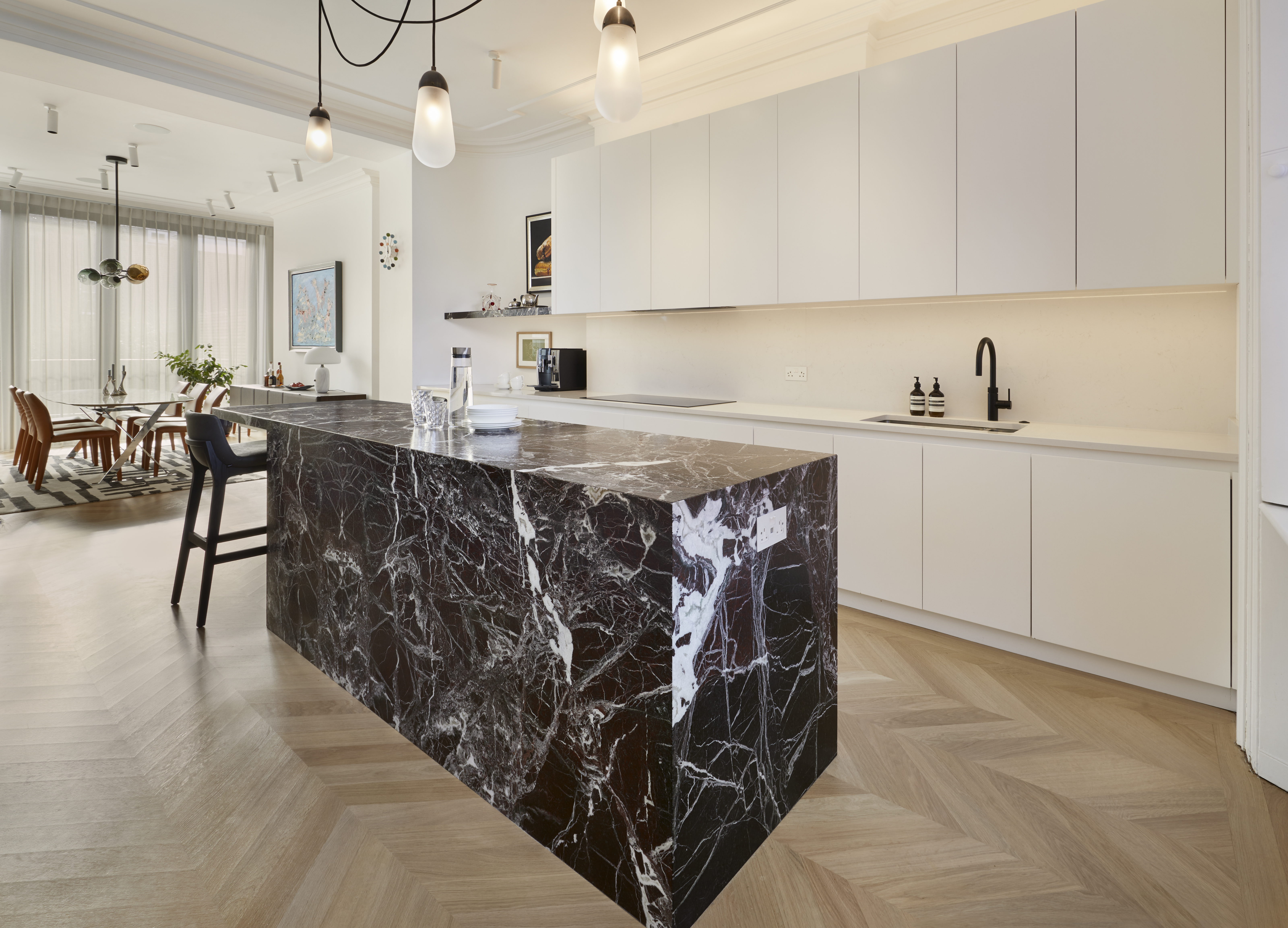 The rear view of a marble-clad kitchen island with white painted cabinets looking towards the dining area