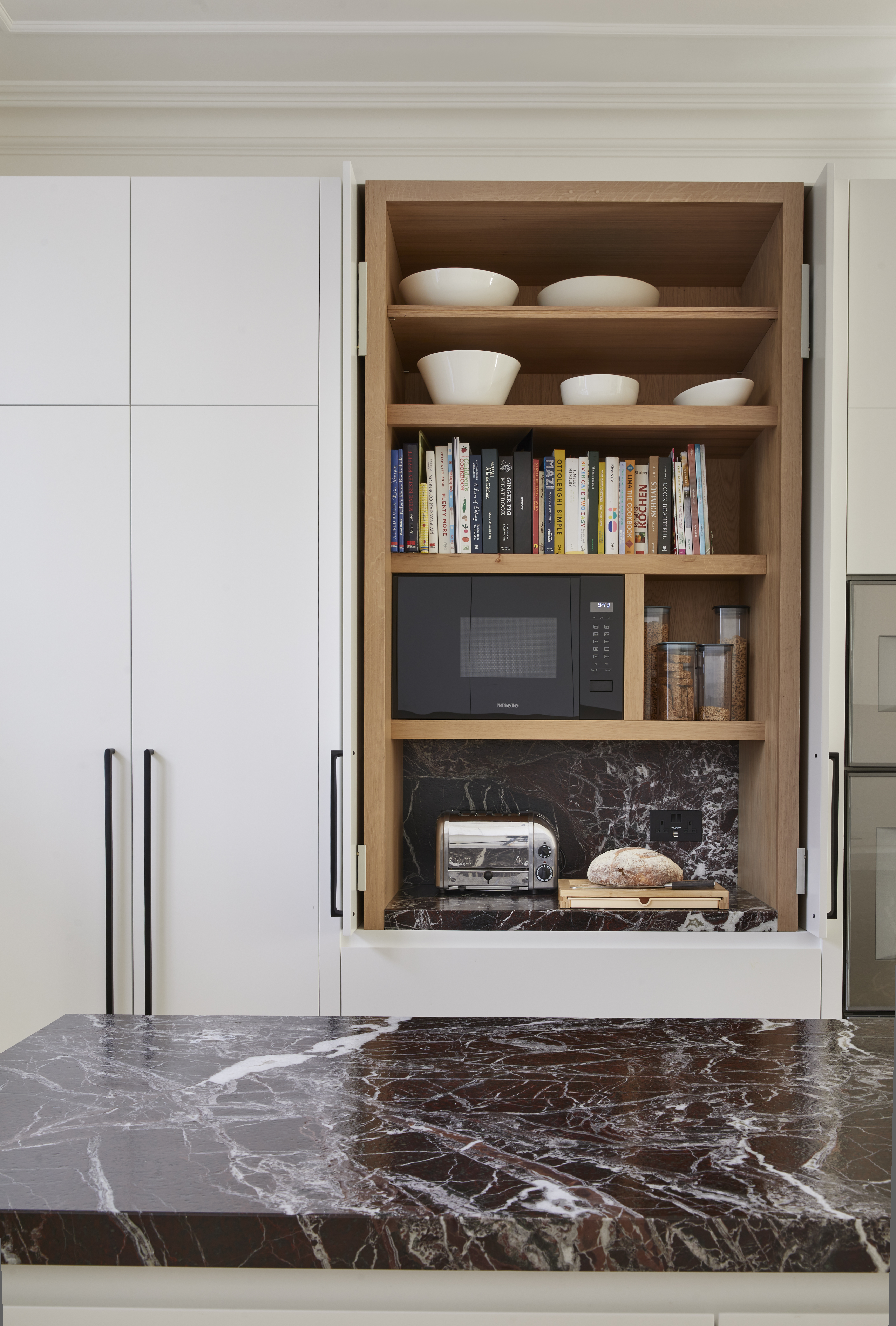 An oak lined breakfast unit with pocket doors in a tall run of white cabinets