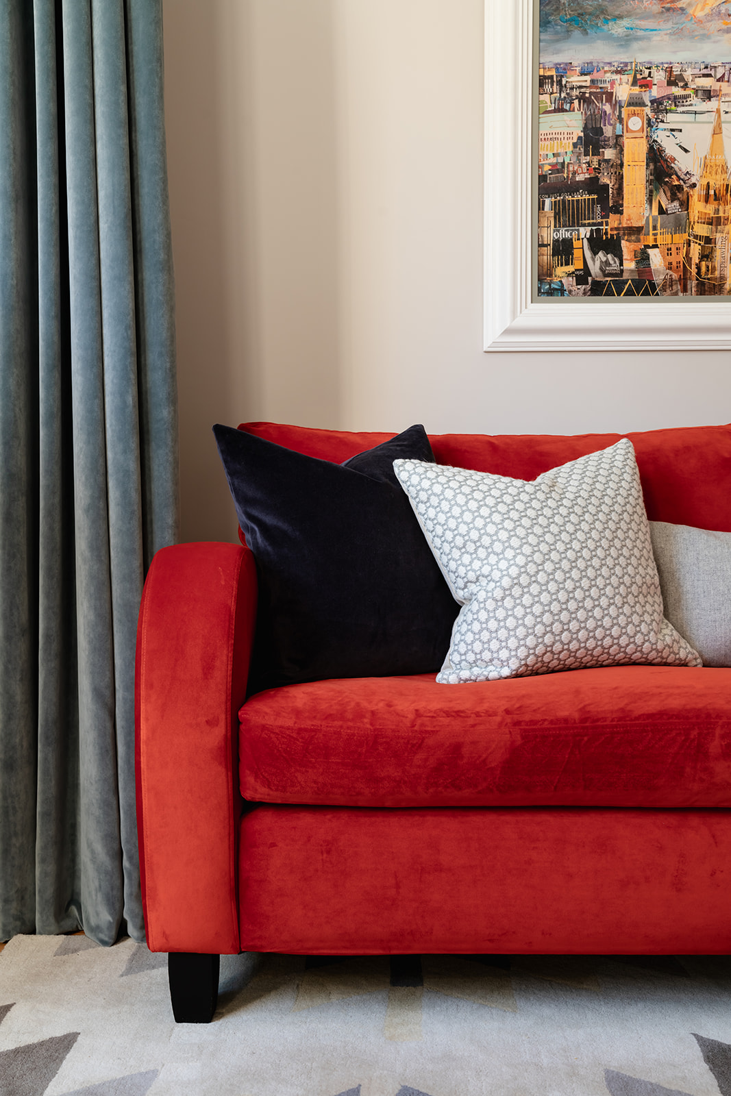 Elegant Richmond riverside home featuring a bold red velvet sofa, layered with plush cushions in neutral and navy tones. Floor-length grey velvet drapery and geometric rug add depth and sophistication, creating a seamless blend of modern minimalism and Art Deco charm.