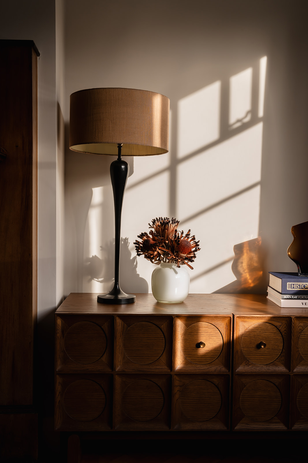 Refined living space in a Richmond family home, showcasing a mid-century inspired wooden sideboard from Soho Home with sculptural details, rich dark grey velvet curtains, and an ambient table lamp. The Art Deco influences bring warmth and timeless elegance to this contemporary interior.