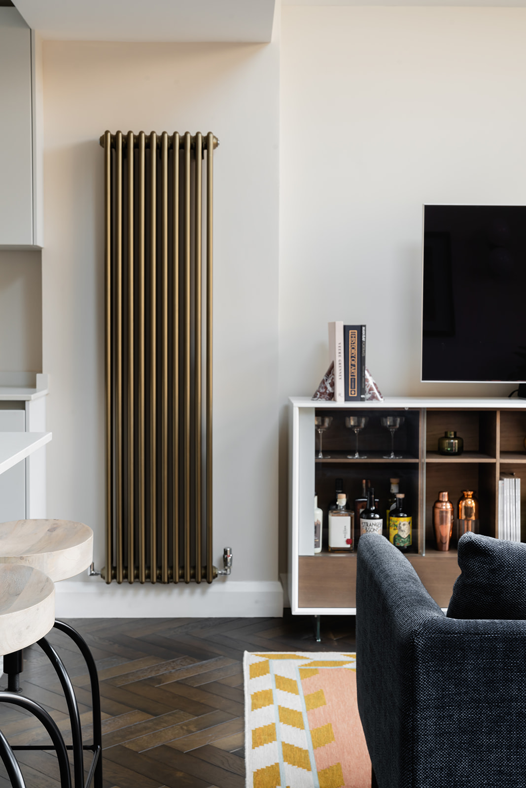 Stylish living area with a statement brass radiator – Blending modern minimalism with Art Deco elegance, this Richmond home showcases a sleek living space featuring a brass vertical radiator, bespoke shelving, and a curated selection of barware.