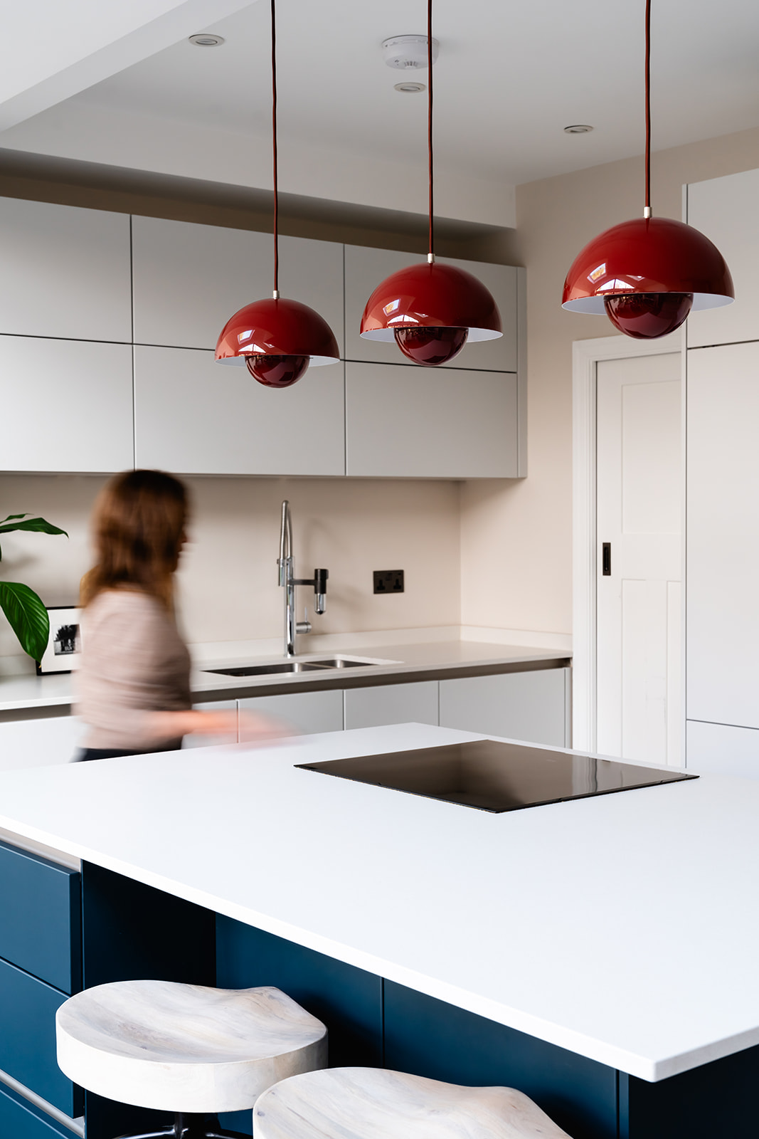 A sleek and modern kitchen in a Richmond riverside home, featuring a striking navy and white island, soft grey cabinetry, and bold red flowerpot pendant lights. A contemporary yet timeless design for effortless family living.