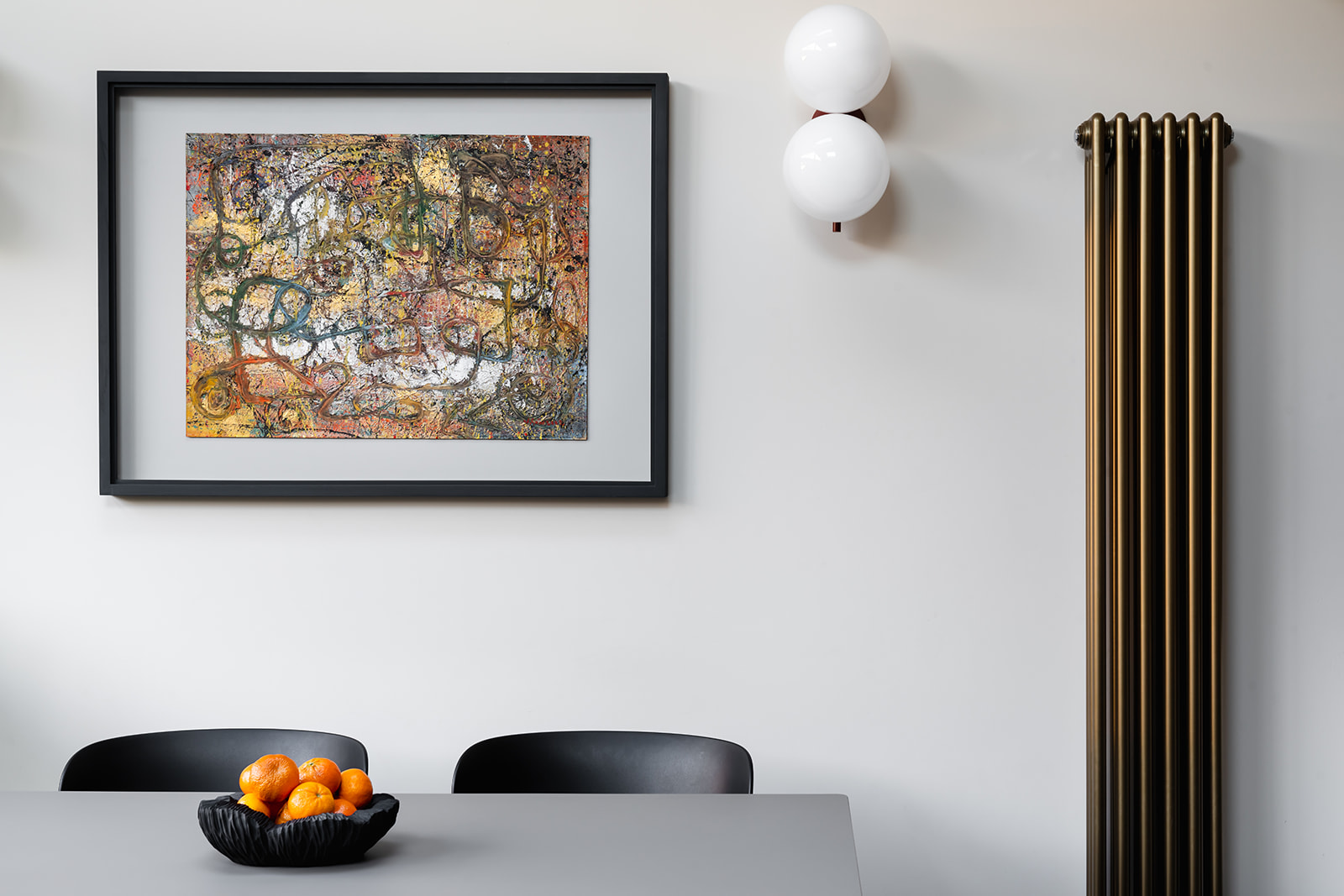 Minimalist dining space with abstract artwork and brass accents – A curated dining area in this Richmond home blends clean lines with statement lighting and a vintage-inspired radiator. Bold artwork adds personality, while warm metallics introduce an Art Deco influence.