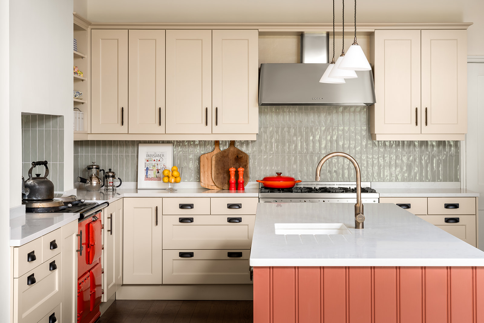 Charming and sustainably refreshed kitchen featuring cream shaker cabinets, a statement red Aga cooker, a painted terracotta island with a white quartz worktop, and soft green backsplash tiles. Thoughtfully designed to blend traditional craftsmanship with modern, eco-conscious choices for a timeless yet responsible interior.