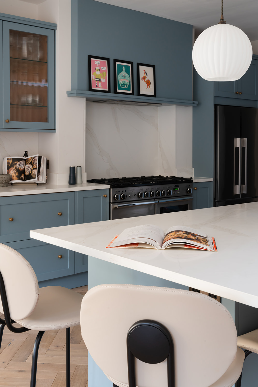 Modern kitchen with a spacious island, soft blue cabinetry (painted in Farrow & Ball’s Selvedge), sleek white quartz countertops, and elegant opaline glass pendant lighting (Pooky Pumpkin) for a contemporary yet timeless design