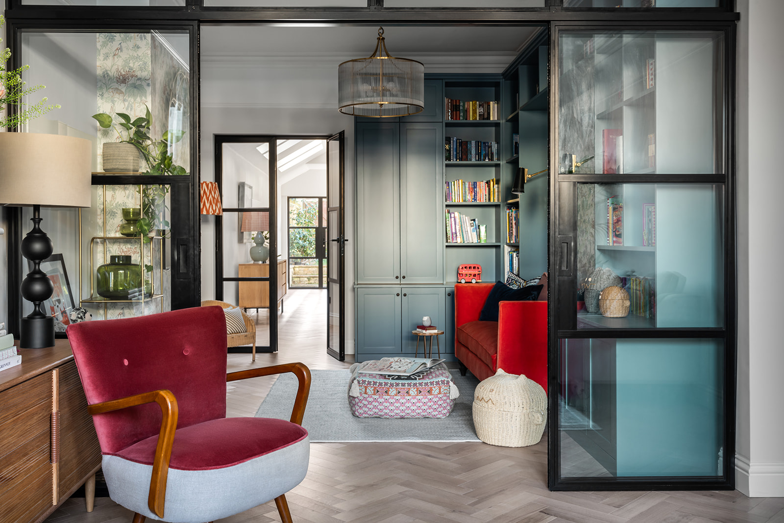 Spacious double living room featuring warm neutral tones, deep grey-blue built-in bookcase and terracotta furnishings, layered textiles, and curated artwork for a cosy yet stylish ambience.