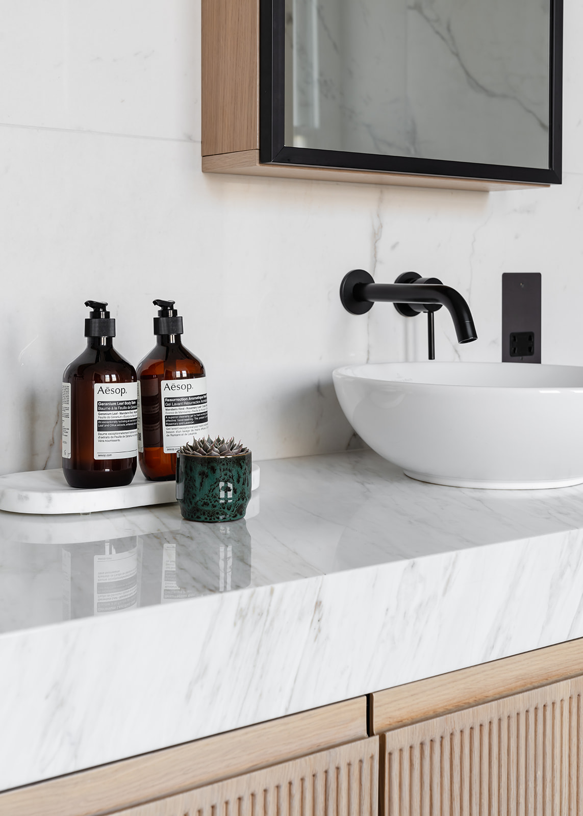 An elegant vanity detail with a marble stone countertop, minimalist Villeroy & Bosch countertop basin, and premium Aesop hand wash. Black brassware contrasts against the light surfaces for a refined finish.