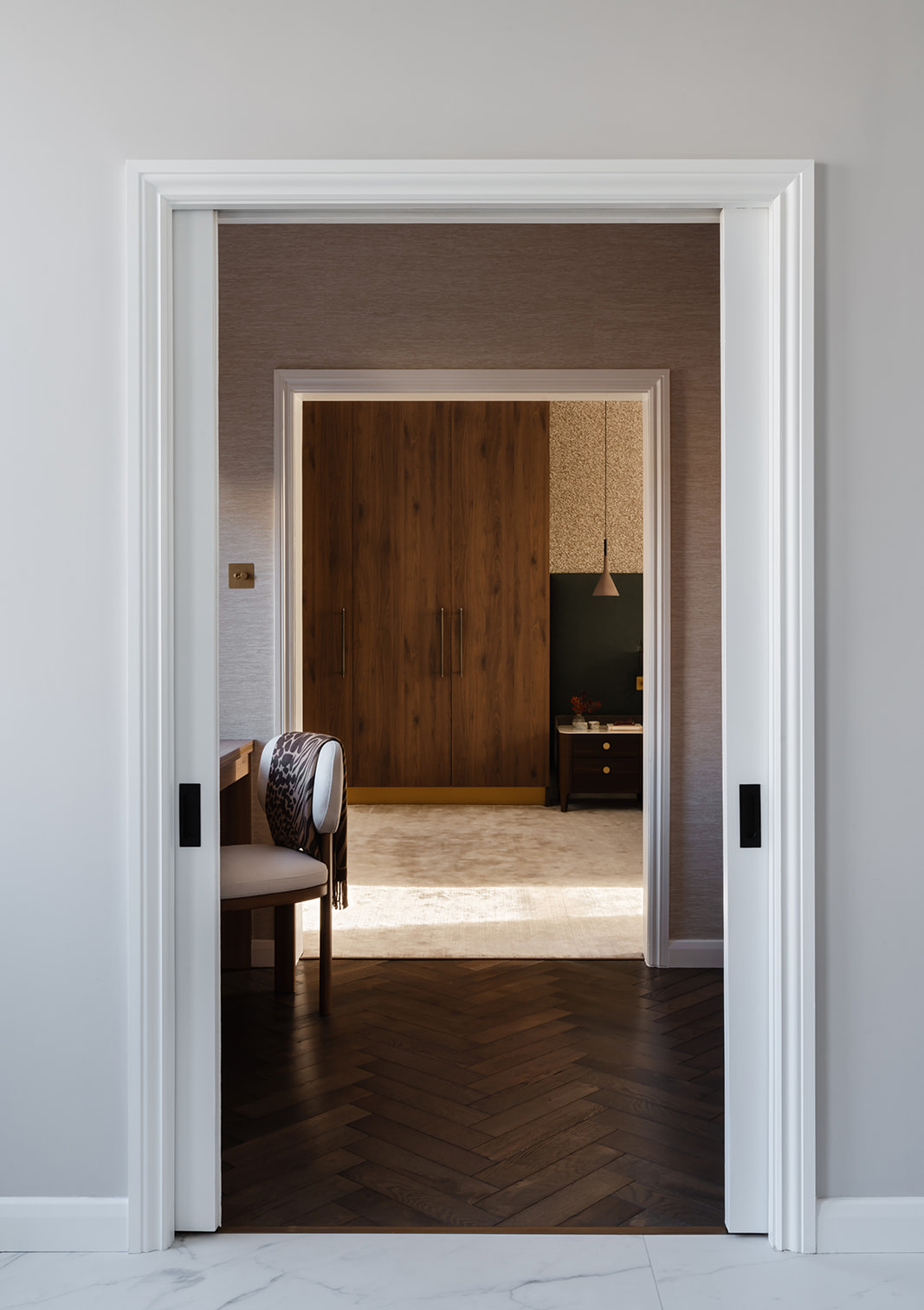 This beautifully framed view from the bathroom through the dressing room into the bedroom showcases a seamless design flow between spaces. Warm wood tones contrast elegantly with Cararra marble flooring and luxurious deep-pile carpet.