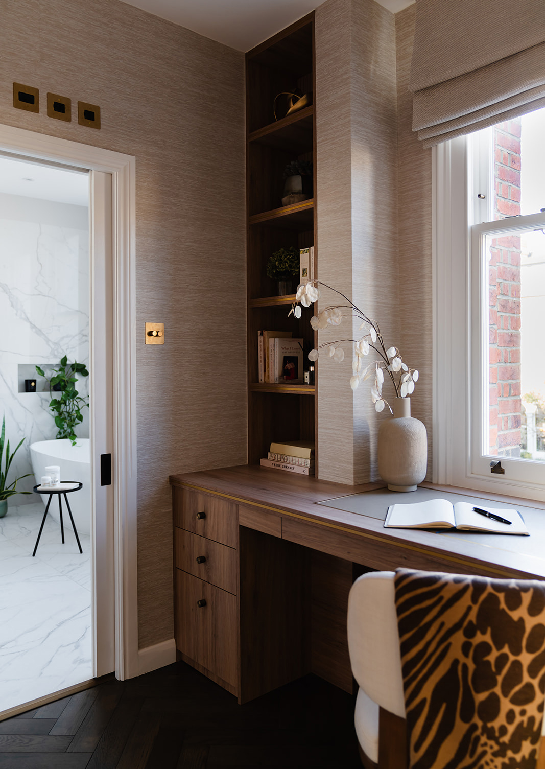 A beautifully designed home office corner with an oak veneer desk, built-in shelving with brass trim, and an upholstered contemporary chair in linen. A warm neutral palette and soft lighting create an inviting and productive workspace.