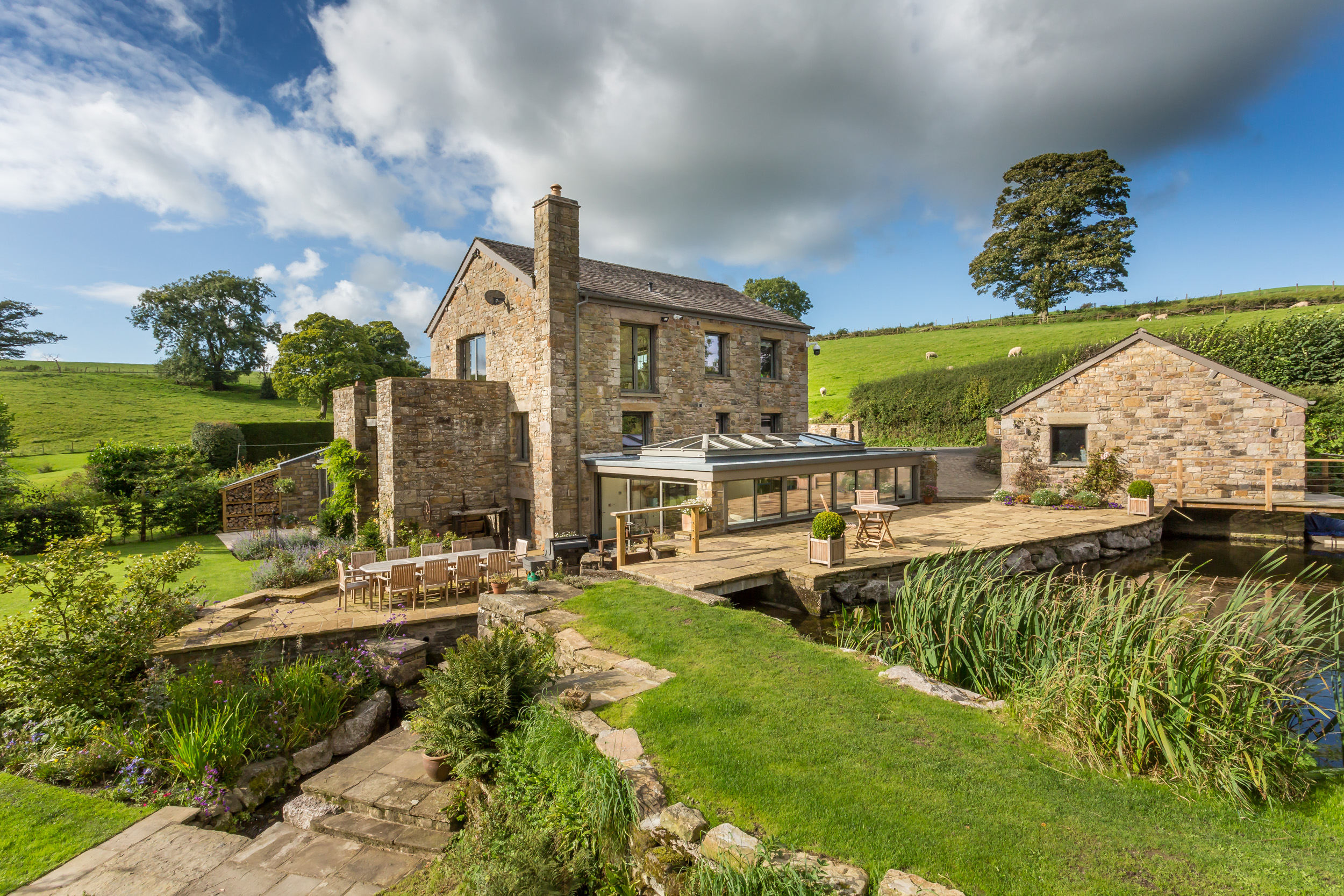 External Image of a Grade II Mill Home Renovation in the Lake District, featuring restored stonework and modern extensions. The building harmonizes with the natural landscape, offering views of the lake and greenery