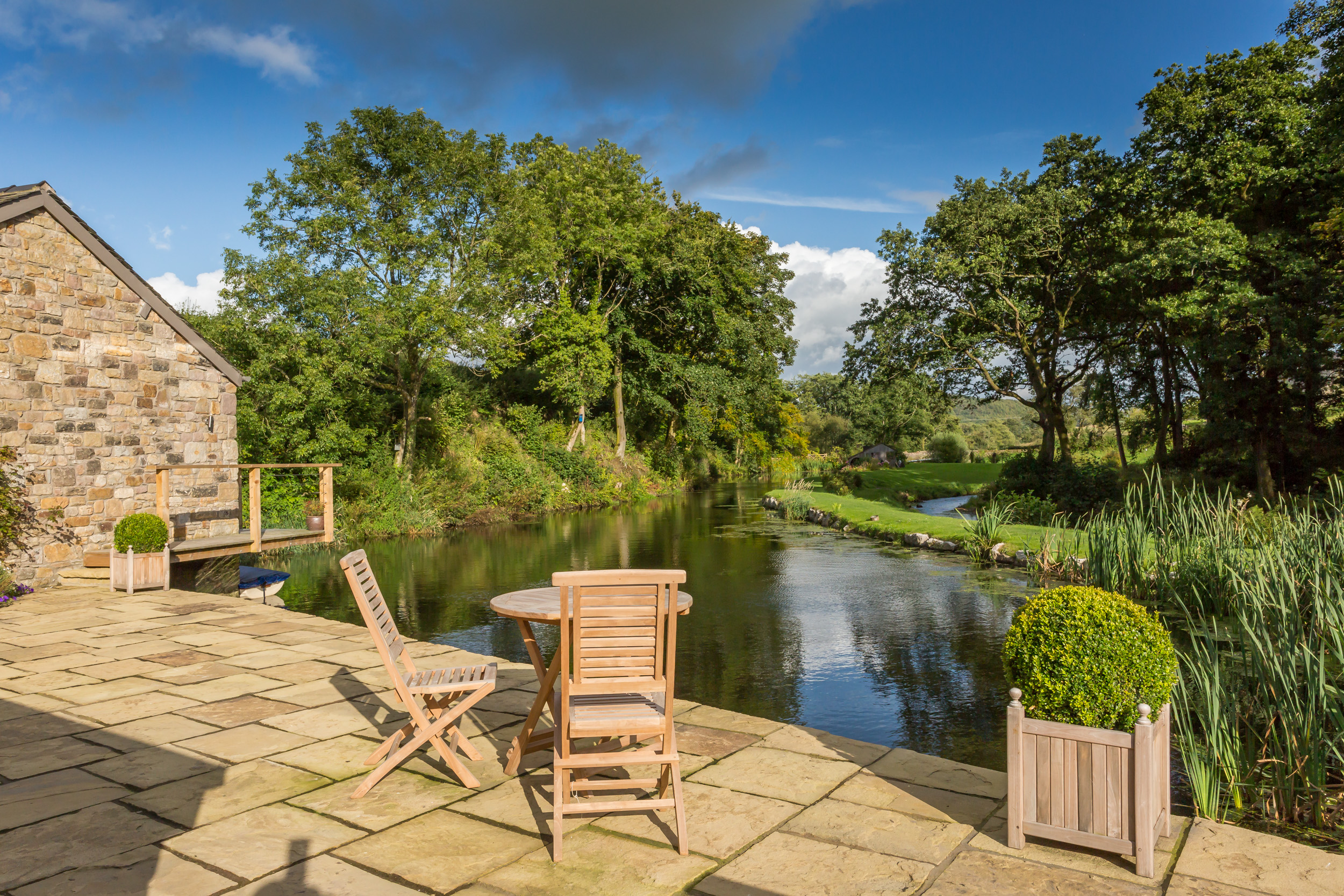 External Image of a Grade II Mill Home Renovation in the Lake District, featuring restored stonework and modern extensions. The building harmonizes with the natural landscape, offering views of the lake and greenery