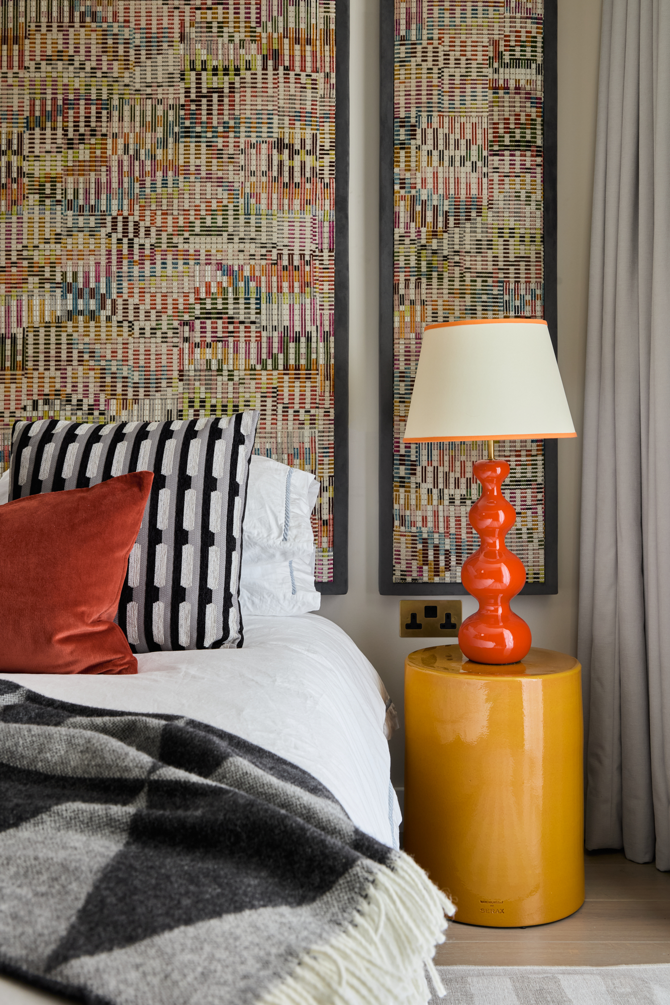 A bold guest bedroom at Triptych Bankside featuring patterned wall panels, bright cushions, and mustard bedside tables, combining colour and texture.