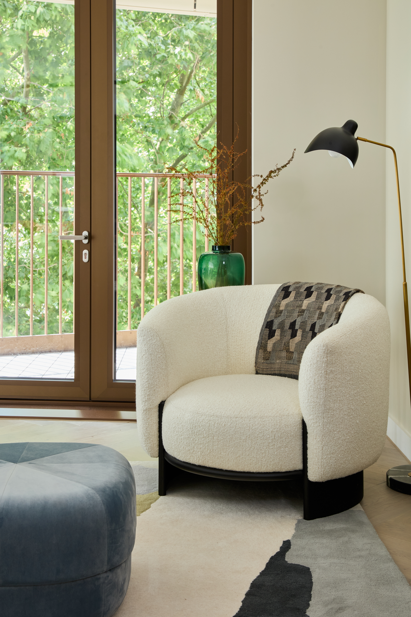 Stylish reading nook in a Triptych Bankside apartment featuring a boucle armchair, statement floor lamp, and a balcony with views over London’s Southbank.