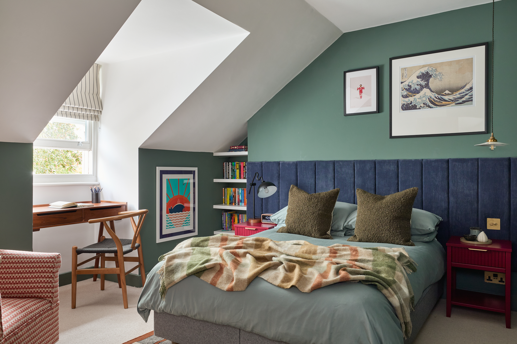 A stylish teenage bedroom featuring a plush blue corduroy headboard, framed artwork, and built-in bookshelves filled with colourful books. A cosy throw blanket drapes over the bed, adding warmth and texture. The contrasting tones of deep blue, forest green, and burgundy create a visually dynamic and inviting space.