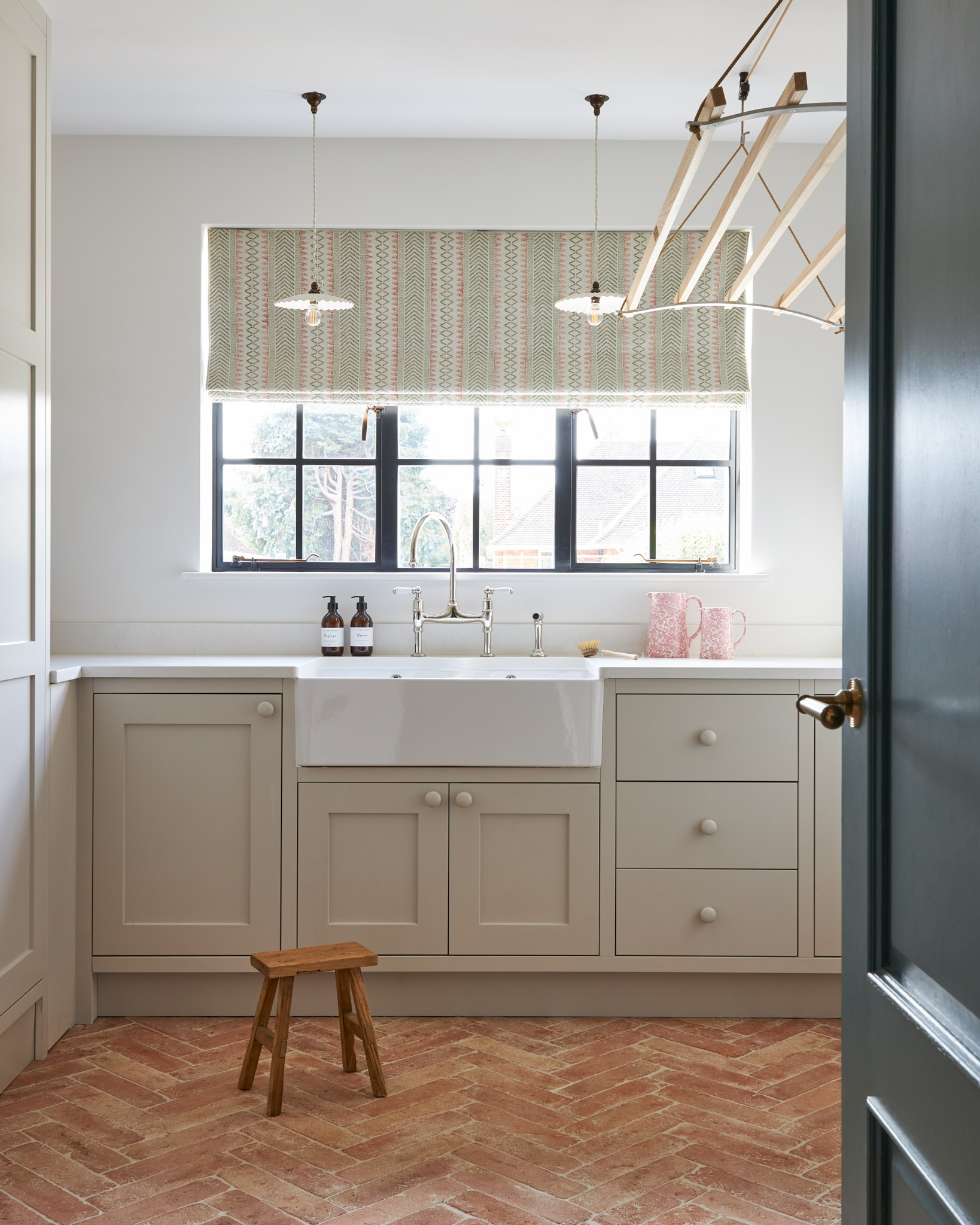 Terracotta herringbone tiled floor utility laundry room with butler sink and painted shaker cupboards