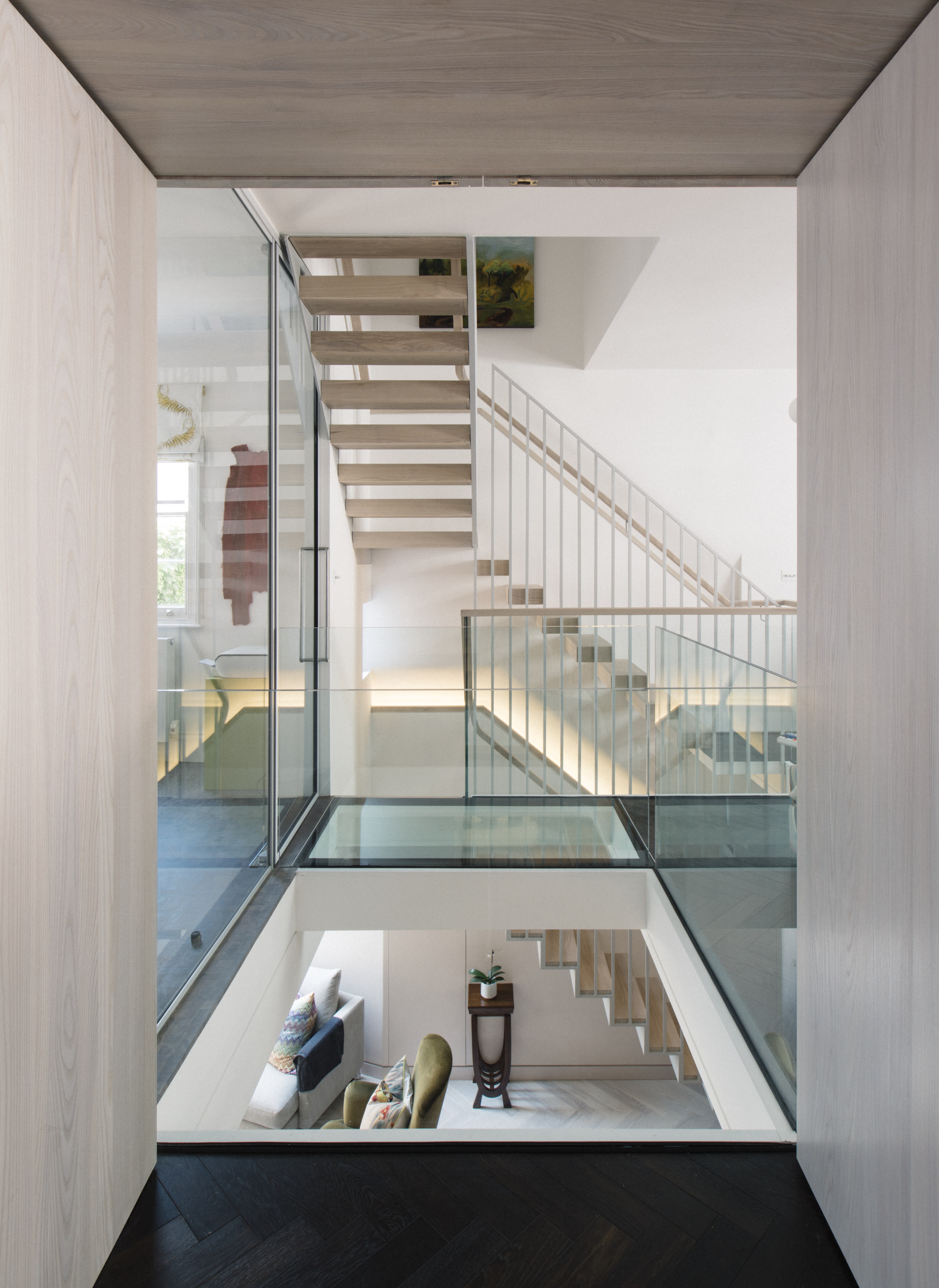 A floating staircase of white oiled ash hovers above the glass bridge and central void, allowing for maximum light