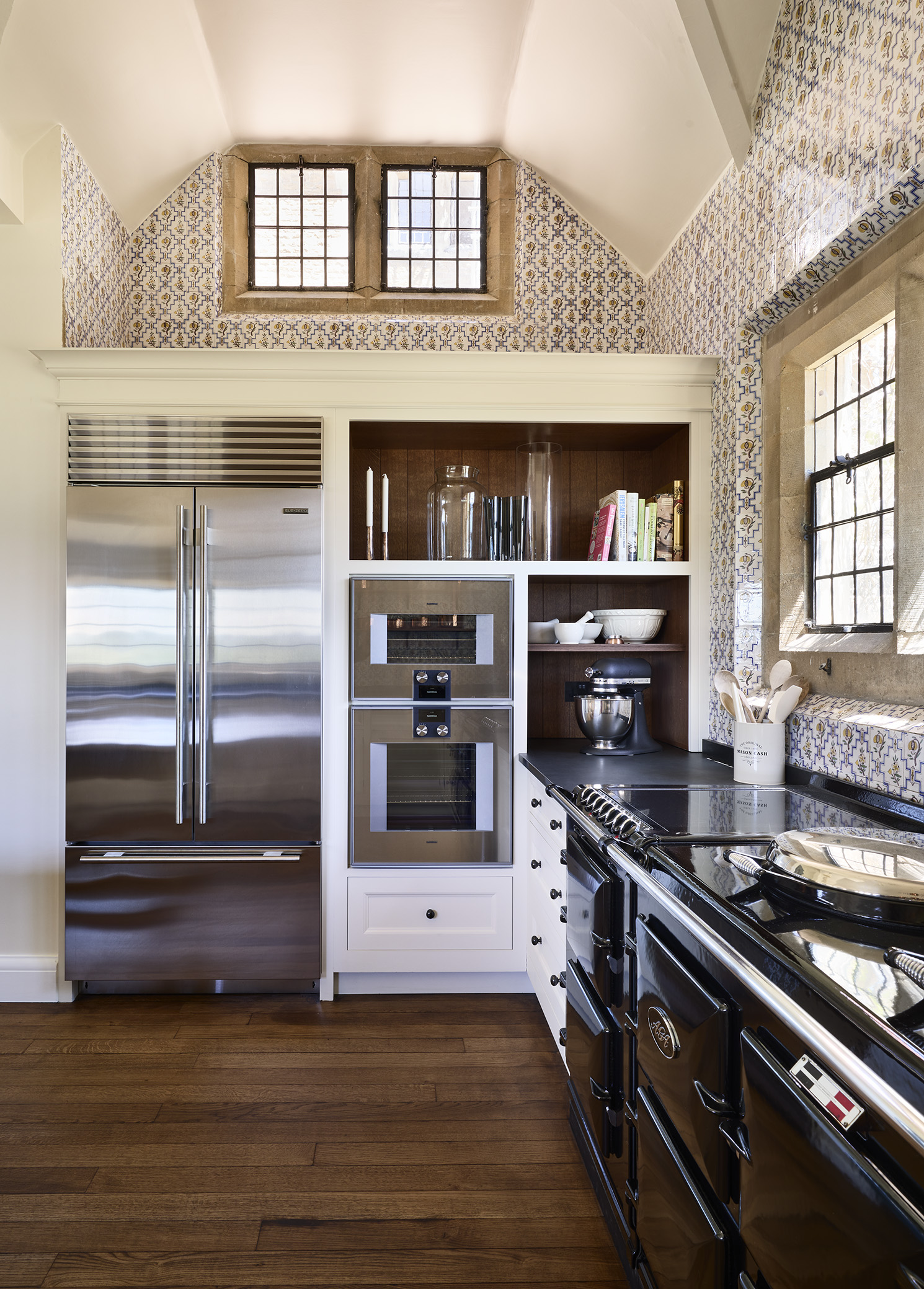 A black AGA range cooker to the right with a run of tall cabinets housing oven and a stainless steel fridge freezer