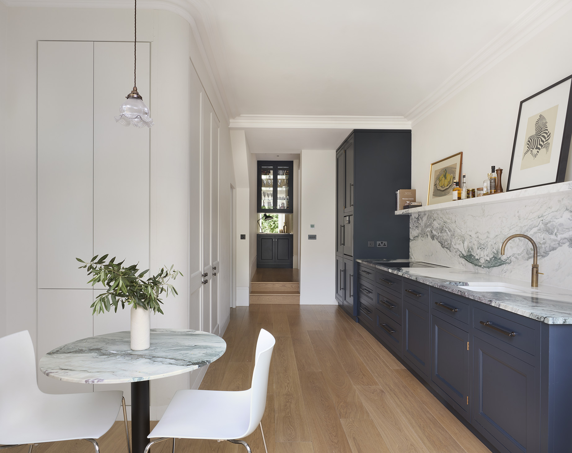 A view through a galley kitchen with dark grey & white cabinets towards a drinks cabinet at the end 