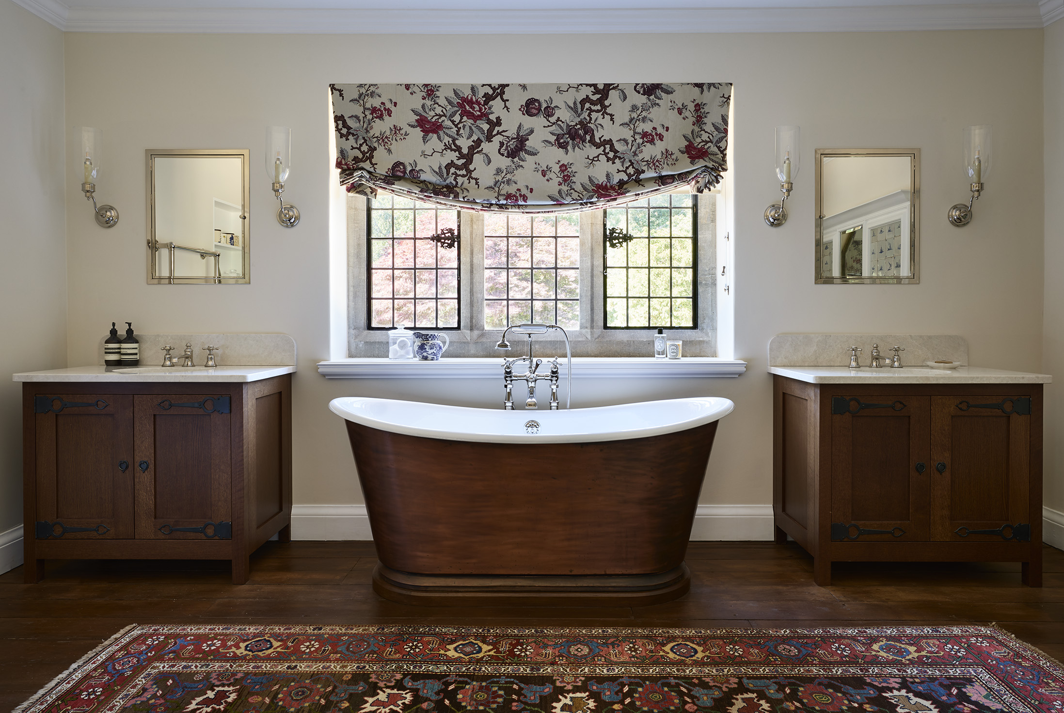 A freestanding dark copper traditional bath with dark oak freestanding vanity units either side 