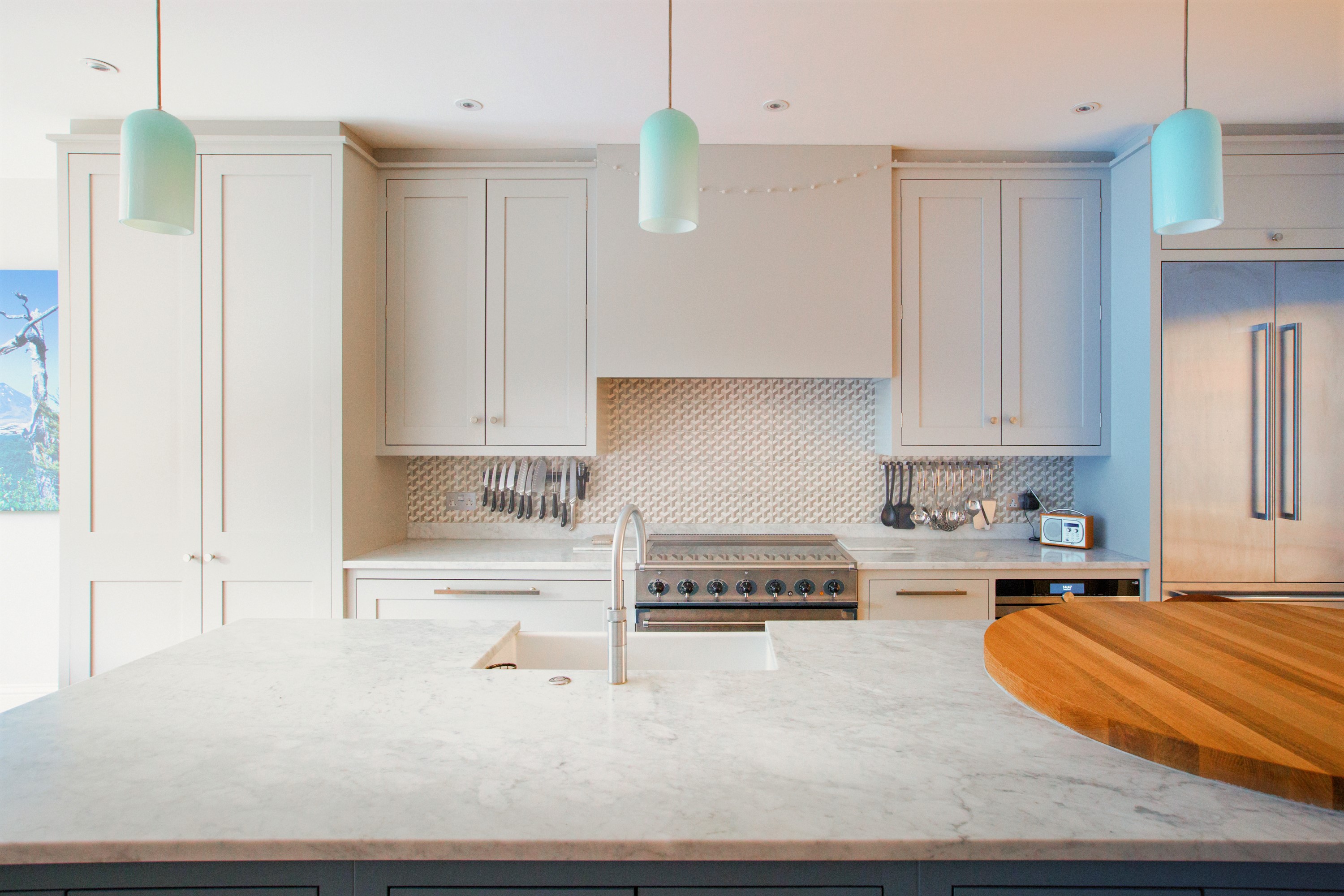 Stepped surfaces of oak and elegant Carrara marble blend seamlessly with the bespoke kitchen, glazed tiles and glass pendant lights