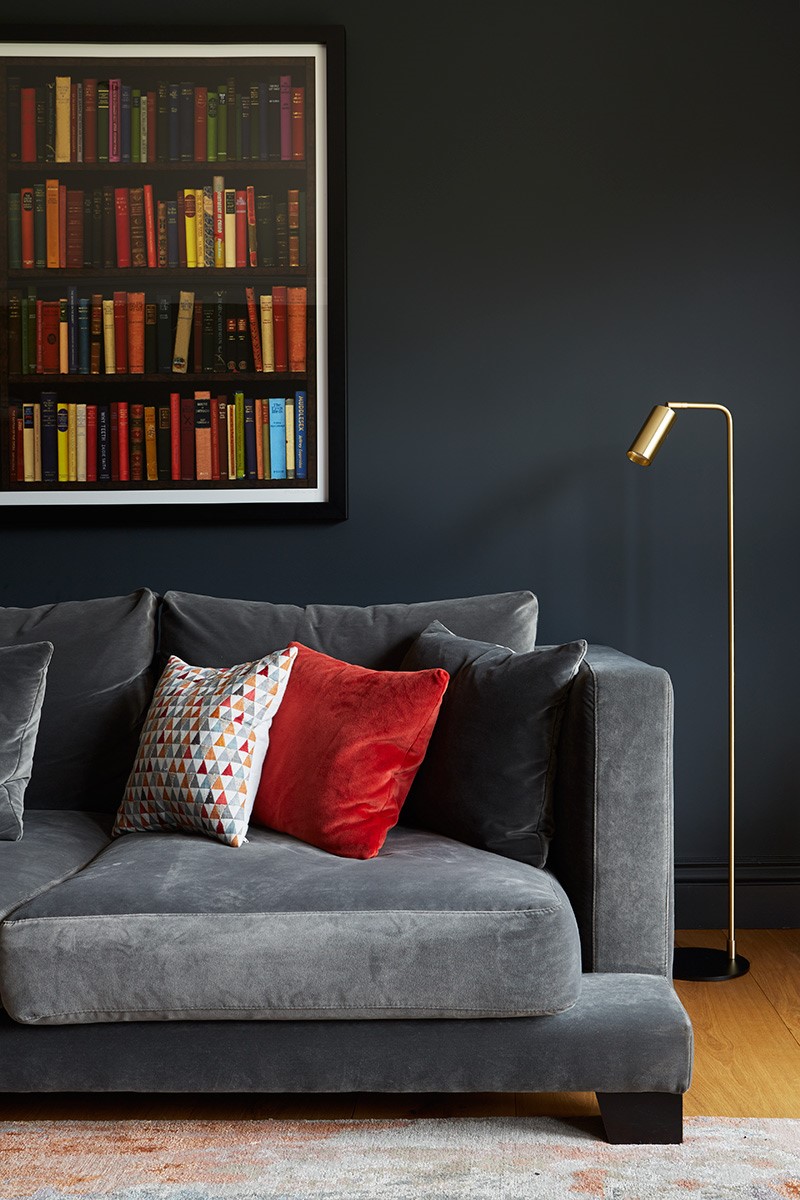 Black walls create a rich family living room, with deep dark grey velvet sofa, accented with orange velvet cushions & brass details.