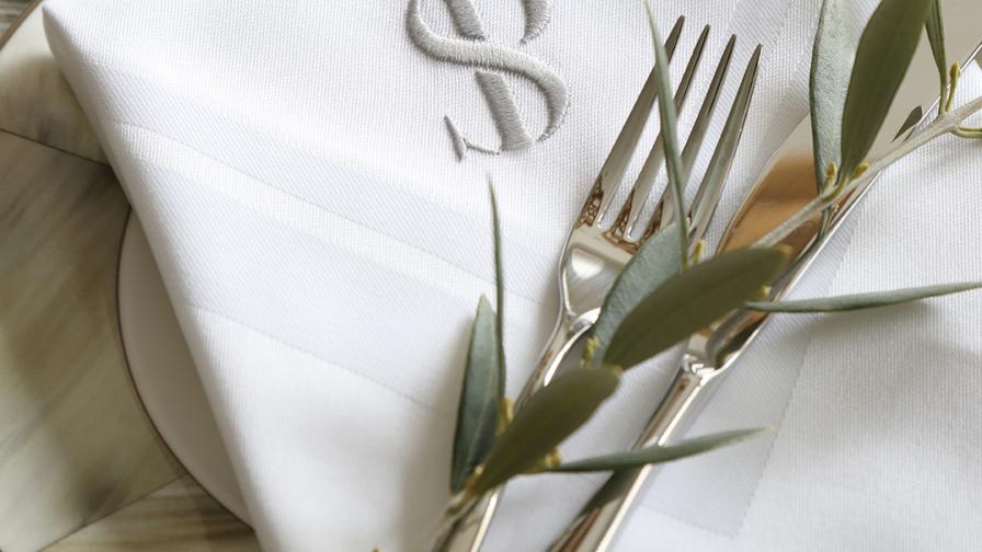 Monogrammed napkin on a patterned plate with fork and olive twig