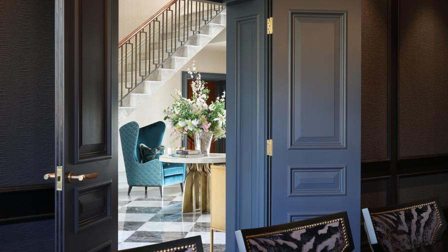 View from dining room through double doors to hall with turquoise wingback chair and staircase