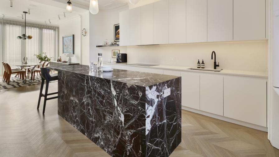 The rear view of a marble-clad kitchen island with white painted cabinets looking towards the dining area