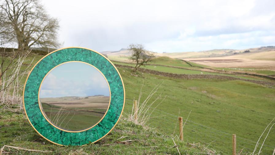 Circular mirror with green frame placed in the Northumberland landscape