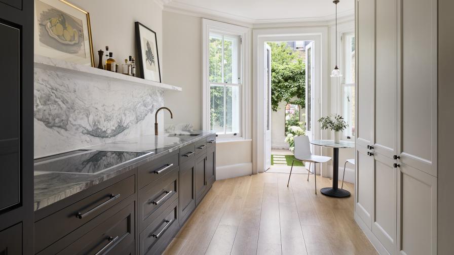 A view through a galley kitchen with dark grey & white cabinets to French doors at one end