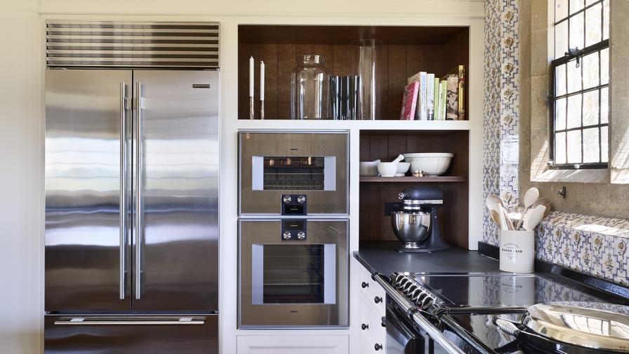 A black AGA range cooker to the right with a run of tall cabinets housing oven and a stainless steel fridge freezer