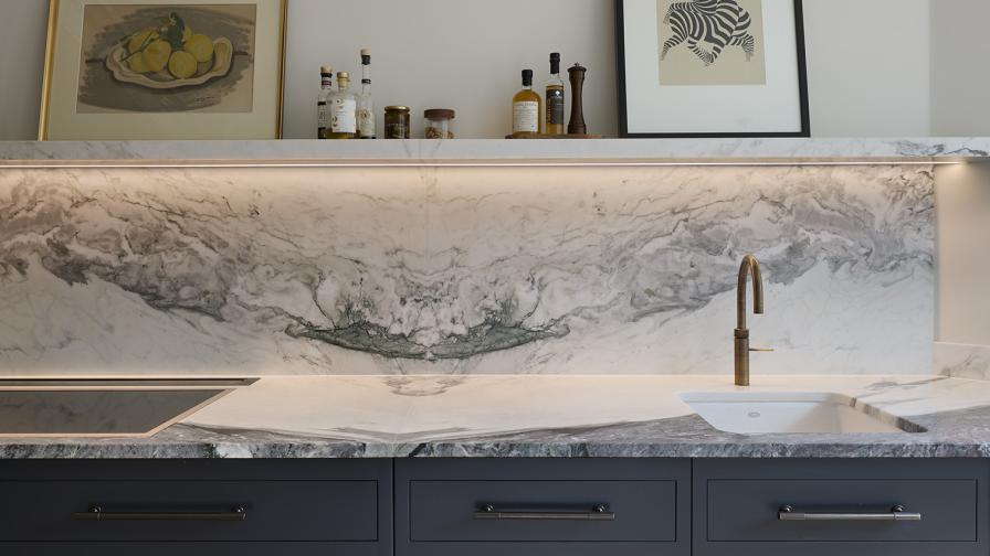 A detail view of a veined marble backsplash with shelf above dark grey base cabinets