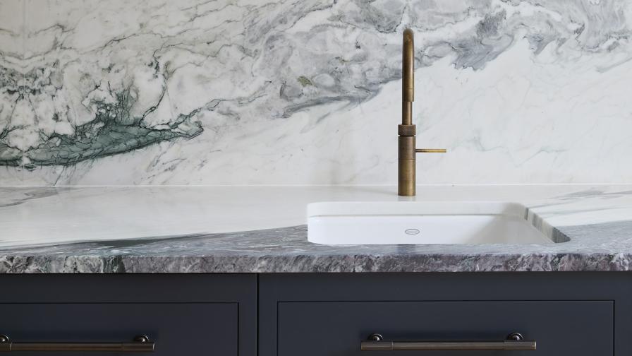 A detail shot of a hot water tap with marble backsplash and dark grey cabinets below.