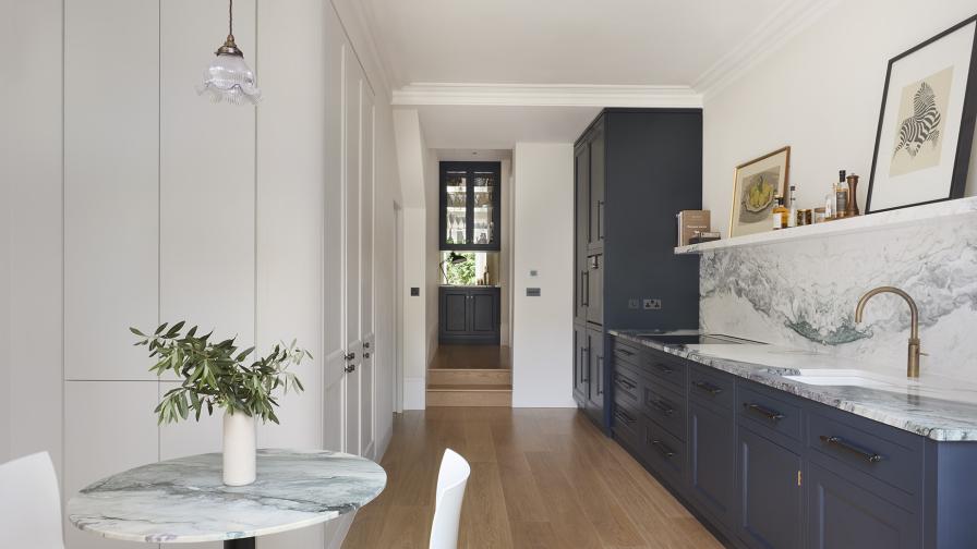 A view through a galley kitchen with dark grey & white cabinets towards a drinks cabinet at the end 