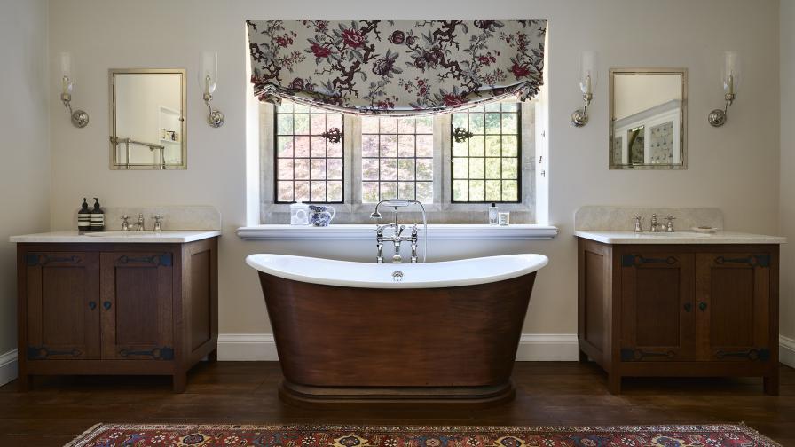 A freestanding dark copper traditional bath with dark oak freestanding vanity units either side 