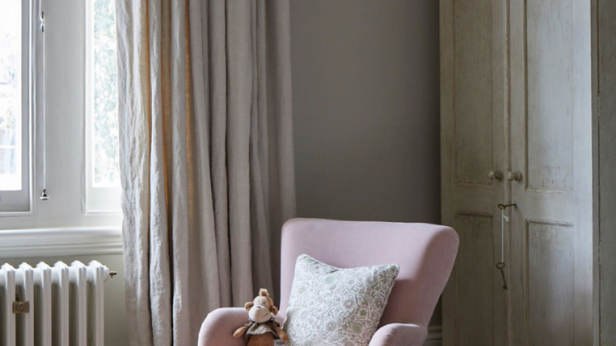 Interior of a bedroom featuring an oak floor, linnen curtains and a soft pink reading chair.